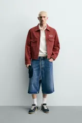 Cazadora cropped fit de Zara confeccionada en tejido de algodón con estructura canvas, de color bordó con efecto lavado. Cuenta con cuello solapa, manga larga con puños abotonados, bolsillos frontales de plastrón con solapa, parche bordado en el pecho y cierre frontal con cremallera.