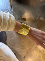 Brazalete rígido de bronce con acabado dorado brillante y diseño ancho y martillado.