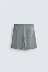 Bermuda de algodón color beige claro, corte relajado (relaxed fit), con cintura elástica ajustable mediante cordón y bolsillos laterales y trasero de plastrón.