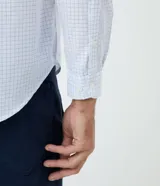 Camisa de corte comfort, manga larga con cuello camisero y cierre frontal de botones. Presenta un estampado de cuadros tipo grid en tonos claros sobre fondo blanco.