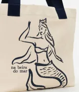 Bolsa de tela color beige con estampado de sirena en azul marino y asas reforzadas del mismo color.