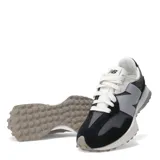 Championes urbanos New Balance modelo 327, con diseño retro inspirado en los años 70. Presentan una combinación de paneles de gamuza negra y malla gris, con el logo 'N' sobredimensionado en color gris claro en el lateral. Incluyen cordones blancos, entresuela de espuma blanca y suela de goma con relieve extendido hacia el talón.