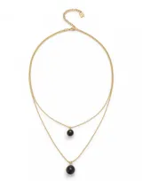 Collar dorado de doble cadena con dije de cristal negro. La cadena superior es más corta y tiene un dije de cristal pequeño, mientras que la cadena inferior es más larga y tiene un dije de cristal más grande.