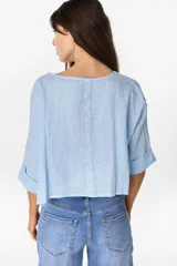 Camisa de lino azul marino, de corte crop y holgado, con cuello redondo, botonadura frontal y mangas amplias con vuelta.