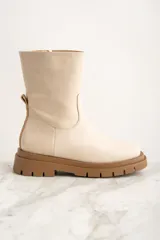 Bota de caña media color crema, confeccionada en cuero. Presenta puntera redondeada, cierre lateral y tirador trasero. Suela track color caramelo.