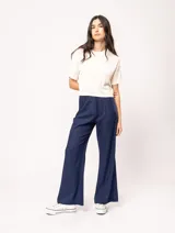 Pantalón de lino color beige, de tiro alto, pierna ancha y levemente acampanada. Tiene pinzas delanteras, elástico en la pretina trasera, cierre delantero y broche interno, bolsillos laterales y dobladillo invisible.