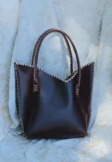 Cartera de cuero mediana con manijas largas, diseño con borde superior en corte en V y terminación artesanal con costuras contrastantes.