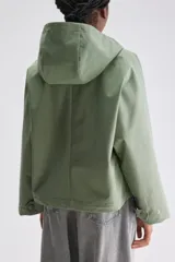 Campera de calce relajado y silueta amplia color verde, con capucha integrada, cierre frontal con cremallera oculta por cartera de broches y bolsillos delanteros con solapa.