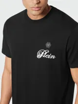 Camiseta negra de manga corta con cuello redondo. Presenta un pequeño parche con el logo de la marca y la palabra "Plein" bordada en cursiva blanca en el pecho.