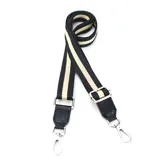 Correa de tela negra con franjas color beige, terminaciones en cuero sintético negro y mosquetones metálicos plateados.