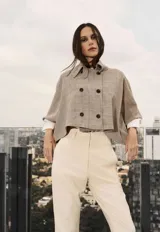 Capa estructurada con diseño de doble botonadura frontal y cuello camisero, confeccionada en tejido con estampado de cuadros tipo tartán en tonos neutros.