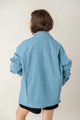 Campera de jean oversize color azul claro, con cuello camisero, cierre frontal con botones y bolsillos frontales. Presenta un diseño de corte amplio y cómodo con mangas largas.