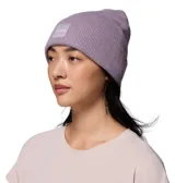 Gorro tipo beanie de punto con puño enrollado, color lila, con parche cuadrado frontal que incluye el logo de la marca.