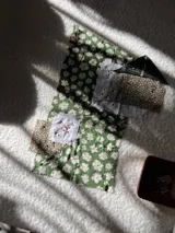 Campera de estilo artesanal confeccionada mediante la técnica de collage con retazos de telas estampadas en tonos verdes y detalles de encaje blanco. Presenta un diseño único y holgado con cierre frontal.