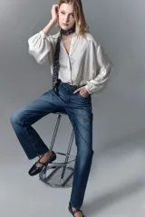 Jean de corte recto y tiro alto confeccionado en denim azul rígido. Presenta un diseño de hotfix brillante aplicado sobre la superficie del pantalón. Cuenta con cierre y botón frontal.