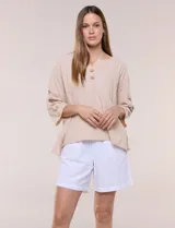 Blusa Erika de algodón con estampado de rayas en tonos azules, rosados y amarillos. Presenta cuello redondo con escote en V y botones frontales, mangas cortas decoradas con una fila de botones en los laterales y dobladillo asimétrico.