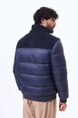 Campera puffer negra con paneles de textura tipo corderito en la parte superior del pecho y hombros. Cuenta con cierre frontal, puños y ruedo acanalados, y un bolsillo vertical con cierre en el pecho.