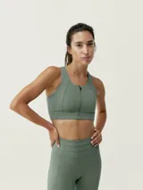 Top deportivo verde con cremallera frontal, de sujeción alta y tejido Shape_Tech con tecnología Performance.
