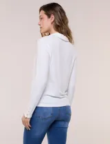 Remera de silueta al cuerpo de tejido de punto acanalado blanco, con cuello polo, abertura frontal con botones dorados y mangas largas con puños abotonados.