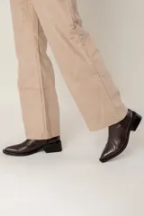 Bota tipo chelsea de caña media con acabado efecto cocodrilo en color chocolate. Presenta paneles elásticos laterales, puntera cuadrada y taco ancho geométrico.