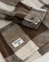 Sobrecamisa de paño con diseño de cuadros grandes en tonos marrón y beige. Presenta cuello clásico, cierre frontal con botones, mangas largas con puños abotonados y dos bolsillos frontales con solapa.