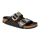 Sandalia Birkenstock modelo Arizona con dos correas anchas de cuero charolado negro y hebillas grandes metálicas doradas. Cuenta con plantilla anatómica de corcho y suela de goma antideslizante.