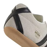 Championes Adidas modelo Tokyo de corte bajo, confeccionados en gamuza color beige con las icónicas tres tiras laterales en cuero negro. Presenta suela de caucho color caramelo y detalle de logo dorado en el lateral.