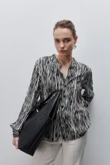 Camisa de calce amplio y fluido de viscosa liviana, con estampado de rayas verticales irregulares en blanco y negro, cuello mao, abotonadura frontal y mangas largas.