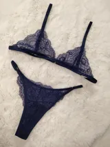 Conjunto de lencería de encaje color azul marino, compuesto por un soutien triangular sin relleno con tirantes regulables y una bombacha colaless ajustable con tiras laterales y detalles de argollas metálicas.