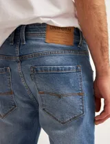 Pantalón de jean azul de corte slim fit, con lavado medio y detalles de desgaste.