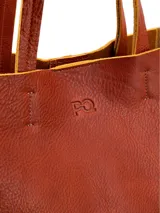 Cartera tipo shopper de cuero color terracota, sin forro y con terminaciones al corte. Cuenta con bolsillo interior con cierre.