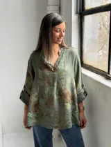 Blusa verde de lino con estampado de flores grandes en tonos marrones y verde oliva, con cuello en V y un botón decorativo central.