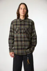 Camisa de manga larga con estampado de cuadros en tonos verde y negro, confeccionada en tela tipo franela. Presenta cuello clásico, cierre frontal con botones y dos bolsillos frontales en el pecho.