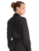 Enterito de crepe negro con cuello camisero, cierre frontal con botones y mangas largas. Presenta cintura elástica con cinto ajustable, bolsillos laterales funcionales y bolsillos simulados en el pecho.