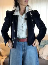 Chaqueta de terciopelo azul marino con hombreras marcadas, mangas largas y bordados florales plateados en el frente. Presenta un diseño estructurado con cierre frontal de botones.