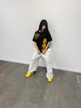 Remera negra de corte regular con estampado gráfico en color amarillo. Presenta inscripciones con estética oriental en la parte superior izquierda y en el lateral derecho. Confeccionada en algodón de alto gramaje con cuello reforzado y grifa de la marca en la manga.