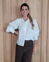 Camisa de lino color blanco, con cuello clásico, cierre frontal de botones y mangas largas abullonadas con puños anchos.