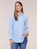 Camisa de calce relajado color celeste, confeccionada en tejido de textura suave y fluida. Presenta cuello camisero y abotonadura frontal, mangas largas con puño ancho y ruedo curvo.