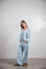 Camisa de tela liviana color celeste, con escote en V y cierre frontal mediante lazos ajustables. Presenta un diseño con volados horizontales en el pecho y mangas largas abullonadas con puños elásticos.
