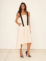 Vestido midi color crema con tirantes anchos negros, corte evasé y bolsillos laterales.