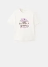 Remera de algodón color blanco, con cuello redondo y mangas cortas. Presenta un estampado frontal con flores en tonos lila y la frase "Self made ready to flourish" en letras negras.