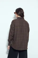 Camisa tipo leñadora de corte oversize, con estampado de cuadros en tonos negro y marrón. Presenta cuello clásico, cierre frontal con botones y mangas largas con puños abotonados.
