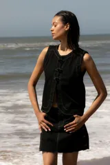 Chaleco de denim celeste sin mangas, confeccionado en algodón. Presenta un cierre frontal con botones forrados en la misma tela y un diseño de bajo redondeado con una abertura central.