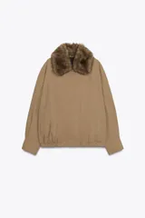 Chaqueta tipo bomber de color beige, con cuello solapa y aplicación extraíble de pelo sintético. Presenta cierre frontal con botones a presión ocultos, bolsillos delanteros y bajo con elástico.