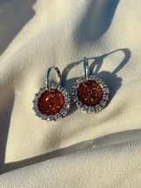 Aros colgantes con forma circular, hechos de resina color lila y borde de strass plateado. El aro es de acero quirúrgico plateado.