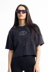 Remera de corte boxy fit, color negro con efecto lavado, de manga corta y cuello redondo. Presenta un logo bordado en el centro del pecho dentro de un óvalo.