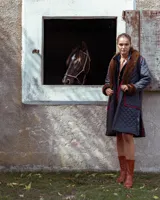 Campera larga acolchada de color azul oscuro, con solapas y puños de piel sintética en tono marrón. Presenta detalles de bordado en crochet de color rojo en los bordes y bolsillos aplicados.