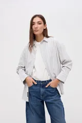 Camisa de corte oversize con diseño de rayas verticales finas en tonos claros. Presenta cuello clásico, cierre frontal con botones y mangas largas con puños abotonados.