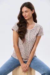 Remera blanca de manga corta con estampado floreado, cuello redondo y detalle de botones frontales.