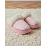 Pantuflas de gamuza color beige con plataforma y forro interior de corderito sintético. Presentan un diseño sin talón con el nombre de la marca bordado en el lateral.